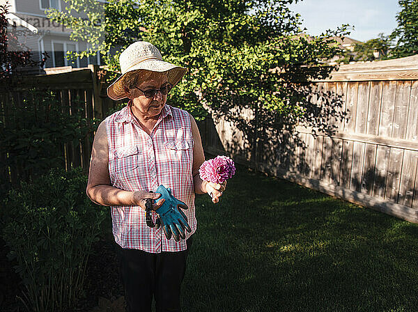 Ältere Frau mit Hut blickt auf einen Strauß frisch geschnittener Blumen in einem Garten.