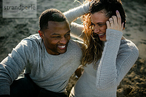 Multi racial couple laugh on beach at sunset