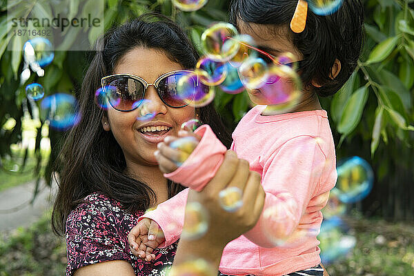 Schwestern spielen und vergnügen sich mit Seifenblasen im Freien