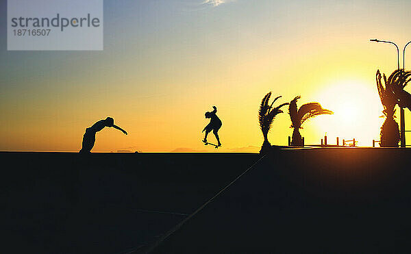 Junger springender Skateboarder reitet  Sommersonnenuntergang