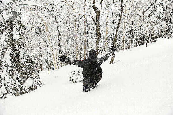 Ein Snowboarder steht mit erhobenen Armen hüfthoch im Backcountry-Pulver