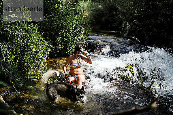 Blonde Frau badet in einem schönen Fluss mit einem Siberian Husky-Hund.