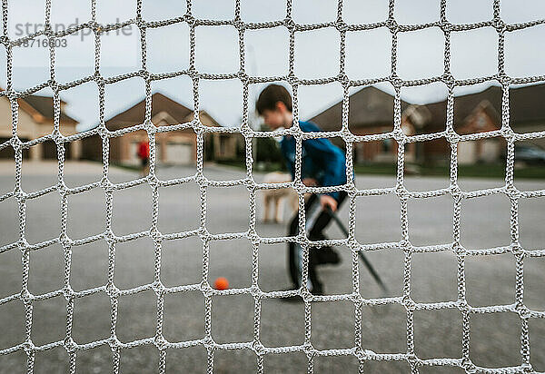 Ein kleiner Junge schlägt einen Ball mit einem durch ein Netz geschossenen Hockeyschläger.