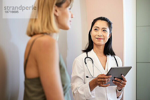 Lächelnder Arzt hält Tablet-PC in der Hand  während er einer Patientin zuhört