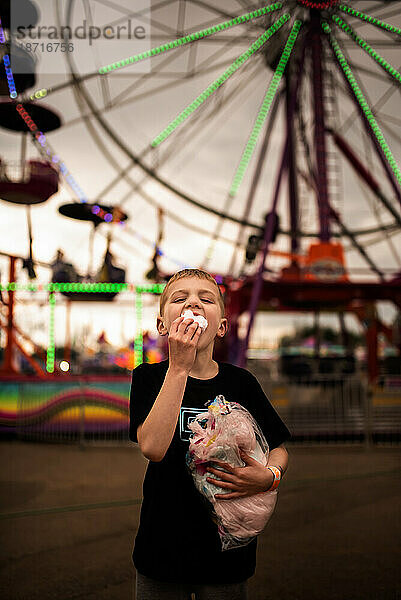 JUNGE ISST ZUCKERWATTE VOR DEM RIESENRAD IM KARNEVAL