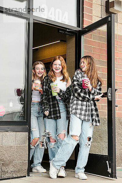 Drei glückliche Teenager-Mädchen verlassen ein Café mit Getränken.