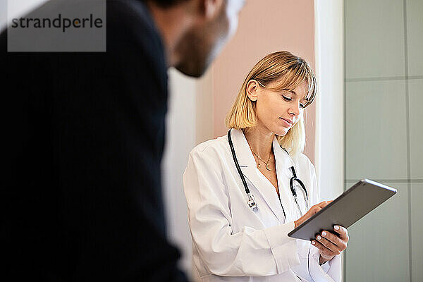 Blonde Ärztin nutzt Tablet-PC von männlichem Patienten in der Klinik