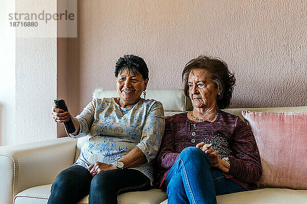 Zwei ältere moderne Frauen sitzen auf dem Sofa und schauen fern