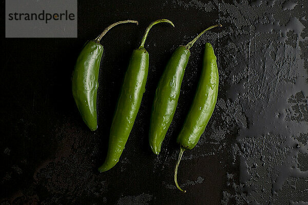 Vier scharfe Bio-Grünpaprika liegen auf einem nassen schwarzen Schneidebrett in einer heimischen Küche in Seattle  Washington.