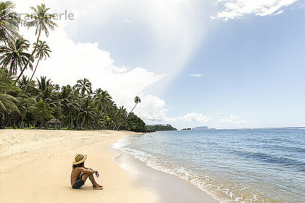 Ein Mann mit Hut entspannt sich am tropischen Sandstrand von Samoa