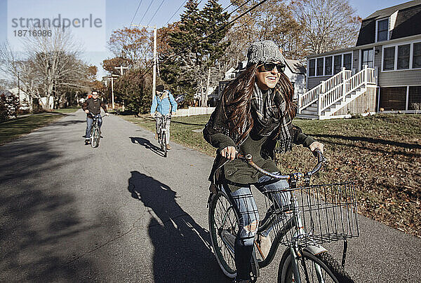 Eine junge Frau lächelt  während sie im Herbst mit dem Fahrrad durch ein Dorf fährt