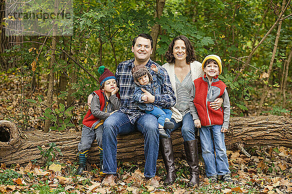Eine lächelnde Familie sitzt zusammen auf einem Baumstamm im Wald