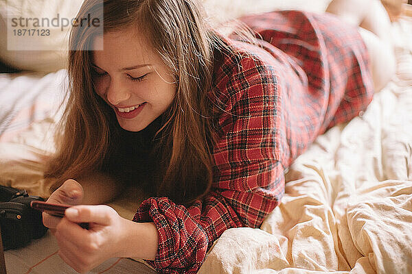 Glückliches Teenager-Mädchen benutzt Smartphone  während es zu Hause im Bett liegt