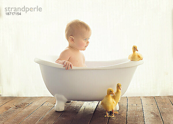 Baby sitzt in einer Badewanne mit Enten