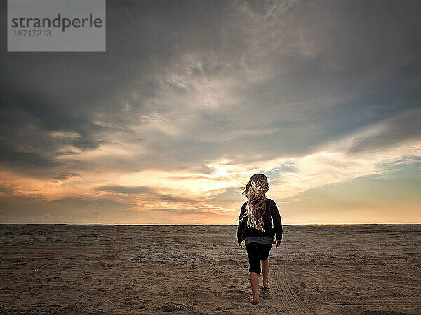 Junges Mädchen läuft bei Sonnenuntergang den Sandstrand entlang