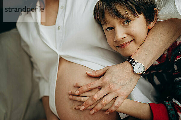 Der Junge umarmt die schwangere Mutter und blickt in die Kamera
