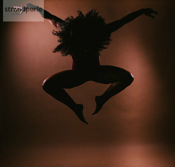 Tänzerin mit lockigem Haar in Sprungtanz-Pose-Silhouette im Studio