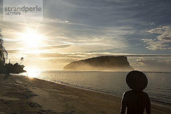 Silhouette eines Mannes mit Hut  der auf den goldenen Sonnenaufgang am Sandstrand starrt