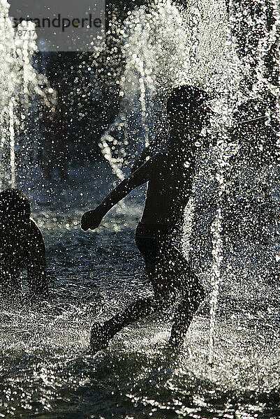 Silhouette von Kindern  die sich während einer Hitzewelle in einem Brunnen abkühlen