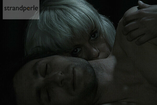 Eine Frau schaut einem Mann auf die Schulter  während sie zusammen im Dunkeln liegen.