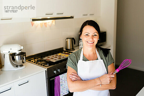 Eine lächelnde Bäckerin in ihrer Küche mit einem Schneebesen