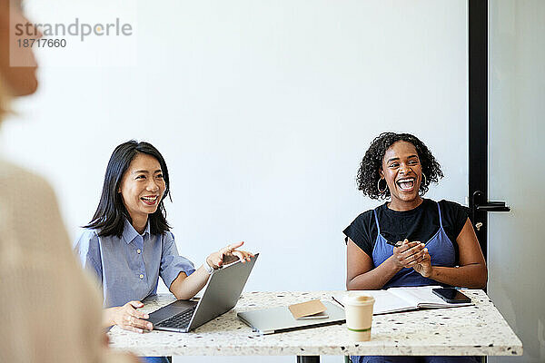 Glückliche Unternehmerin sitzt neben einem Kollegen mit Laptop im Café