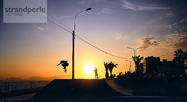 Silhouette eines jungen springenden Skateboardfahrers beim Reiten  Sommersonnenuntergang