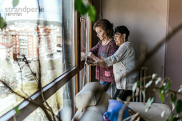 Zwei moderne ältere Frauen beobachten Menschen  die am Fenster vorbeigehen