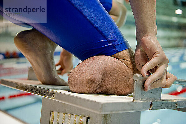 Ein Athlet  der nur ein Bein hat  bereitet sich beim Schwimmtraining auf den Start vom Startblock aus vor.