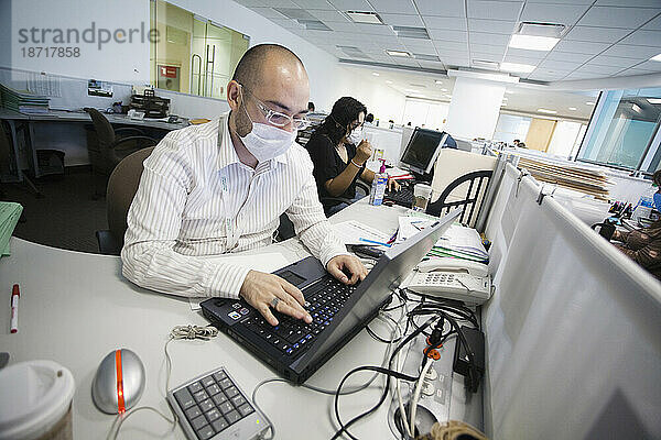 Ein Mann arbeitet mit seinem Computer und trägt eine Maske und Linsen in einem Büro während der Schweinegrippe-Epidemie in Mexiko-Stadt  DF  Mexiko
