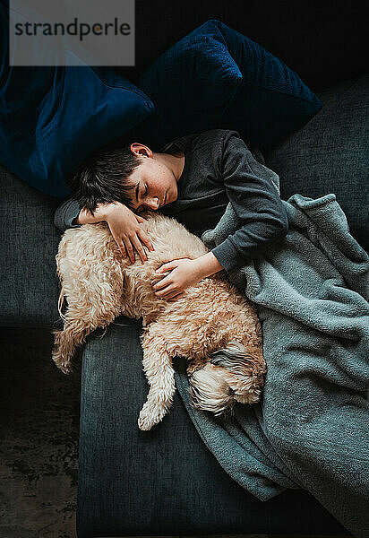Blick von oben auf einen Jungen und einen flauschigen Hund  die zusammen auf dem Sofa schlafen.