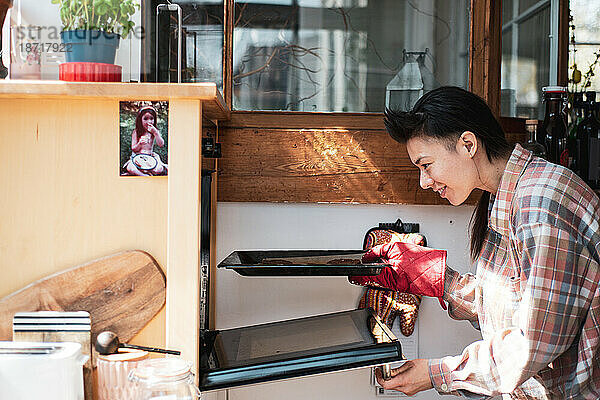 Ein junger Asiate stellt zu Hause ein Tablett mit hausgemachten Keksen in den Ofen