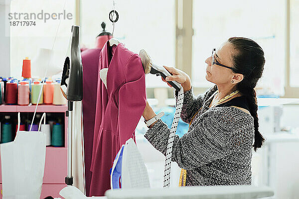 Ältere Frau mit Brille bügelt ein Kleid in einem Modedesignstudio
