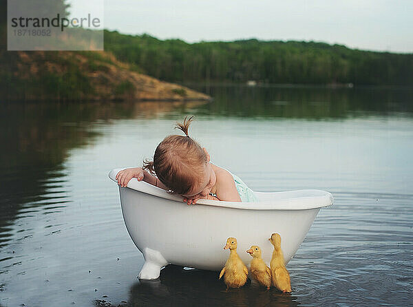 kleines Mädchen in einer Badewanne im See mit drei Entenküken