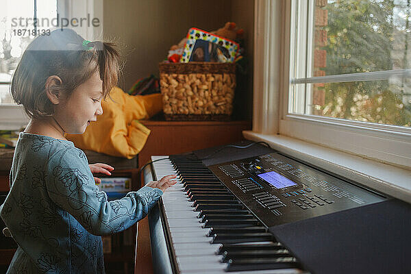 Porträt eines süßen kleinen Kindes  das vor einem Fenster Klavier spielt