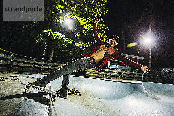 Seitenansicht eines Mannes  der nachts im beleuchteten Skatepark Skateboard fährt  Jimbaran  Bali  Indonesien