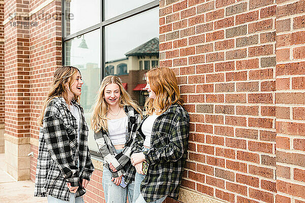 Drei glückliche Teenager-Mädchen stehen draußen und reden.