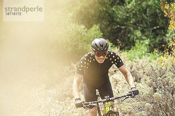 Oberkörper-Actionfoto eines lächelnden männlichen Mountainbike-Radfahrers im Wald