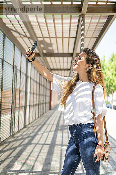 Porträt einer schönen jungen Frau  die mit einem Smartphone ein Selfie im Park macht