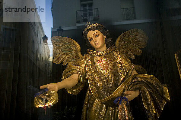 Eine Statue des Heiligen Erzengel Raphael sitzt hinter einem Fenster  während sich die Stadt Cádiz in Andalusien  Spanien  spiegelt.