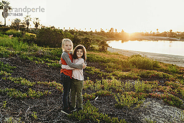 Kleine Jungen und Mädchen umarmen sich am Strand bei Sonnenuntergang