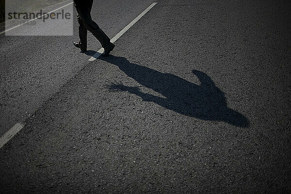 Der Schatten eines Mannes wird geworfen  als er eine Straße überquert  nachdem er wilden Spargel in der Nähe des Dorfes Villamartin  Provinz Cádiz  Andalusien  Spanien  gepflückt hat.