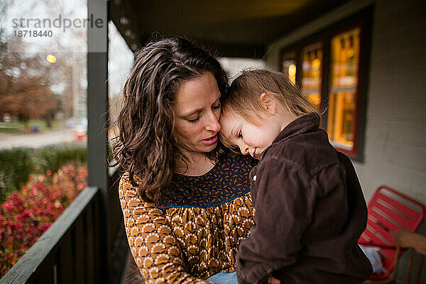Eine Mutter hält ihr Kind auf der Veranda und legt seinen Kopf zärtlich auf sein Kind