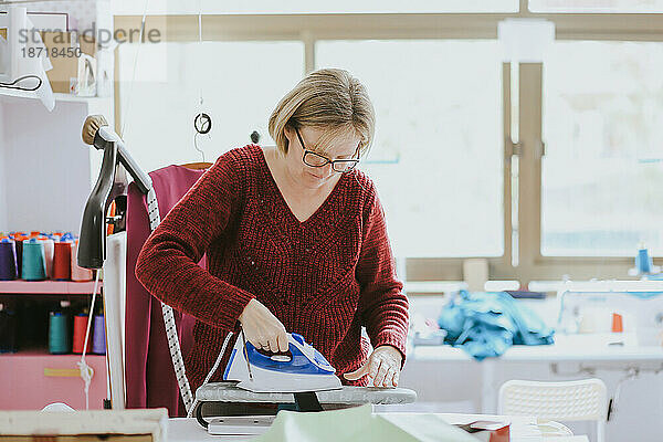 Ältere Frau mit Brille bügelt in einem Modedesignstudio