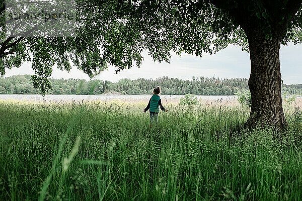 Junges Mädchen steht mitten auf einem Feld und blickt auf das Wasser