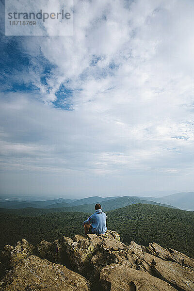 Ein junger Erwachsener sitzt auf einer Klippe mit Blick auf eine weite Bergkette in VA.