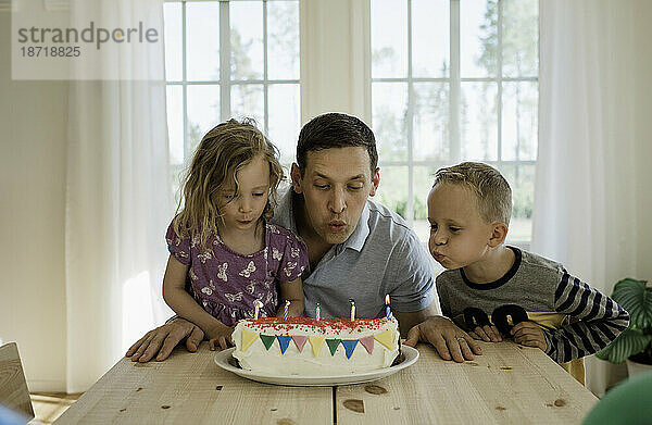 Ein Vater bläst mit seiner Tochter und seinem Sohn Kerzen auf eine Geburtstagstorte