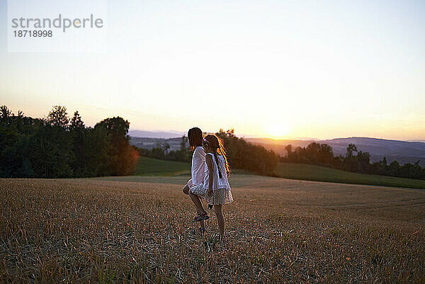 Zwei junge Mädchen laufen im Sommersonnenuntergang über ein Feld