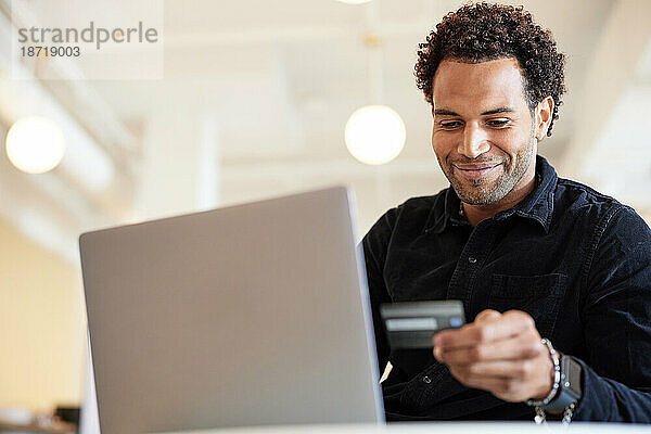 Lächelnder Geschäftsmann hält Kreditkarte am Laptop im Büro