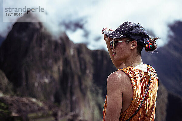 Androgyne Frau mit Mütze blickt auf die Ruinen von Machu Picchu